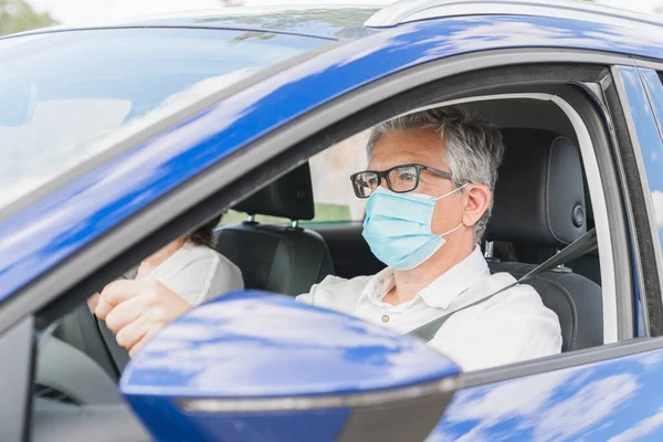 Yeni normal. Tıbbi maskeli bir sürücü bir yolcuyla araba kullanıyor. Sağlık koruması. Arabadaki aile maske güvenliği ve salgın hastalık konseptiyle korunuyor. Coronavirus cihazları. Sosyal uzaklık.