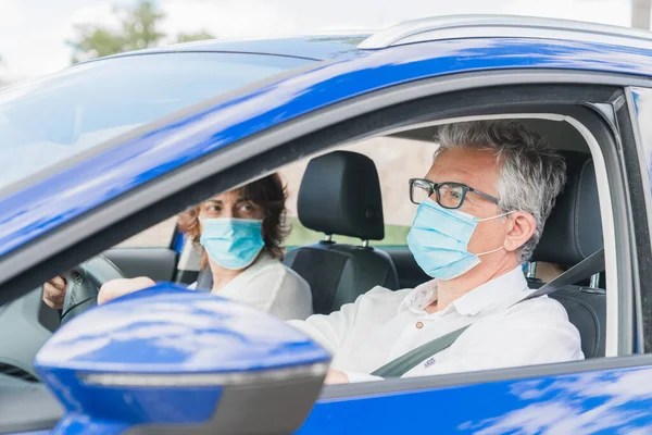 Yeni normal. Tıbbi maskeli bir sürücü bir yolcuyla araba kullanıyor. Sağlık koruması. Arabadaki aile maske güvenliği ve salgın hastalık konseptiyle korunuyor. Coronavirus cihazları. Sosyal uzaklık.