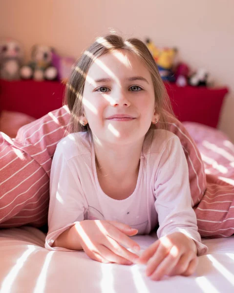 可爱的小女孩早上在床上醒来 阳光透过百叶窗照在孩子的脸上 检疫期间在家里的业余时间 舒适的家无忧无虑的童年 — 图库照片
