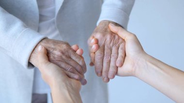 Genç kadınlar, yaşlı bir insanın ellerini nazikçe tutarak, rahatlık, destek ve bağlılık teklif ederek, nesiller arası bakımın iç açıcı bir göstergesi olarak ellerini tutarlar.