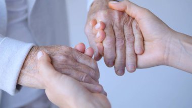 Hemşirelerin ellerini nazikçe yaşlı bir insanın kırışık ellerini tutarak rahatlık, empati ve sağlık hizmetlerinde tıbbi yardım sağlıyorlar.