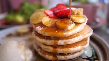 Bal, üzerine muz dilimleri ve yanında bir kepçe dondurma ve tahıl gevreğiyle servis edilen çilekli krep yığınının üzerine dökülüyor.