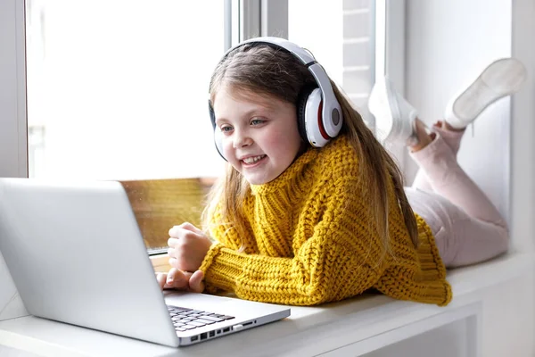 Evde dizüstü bilgisayar kullanan tatlı bir kız. Eğitim, çevrimiçi eğitim, evde öğrenim, okul çocukları yaşam tarzı konsepti. Evdeki kız internet üzerinden arkadaşlarıyla iletişim kuruyor. Çocuklar uzaktan öğreniyor.