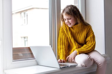 Evde dizüstü bilgisayarlı güzel bir kız pencereye bakıyor ve gülümsüyor. Evdeki kız internet üzerinden iletişim kuruyor. Çocuklar uzaktan öğreniyor.