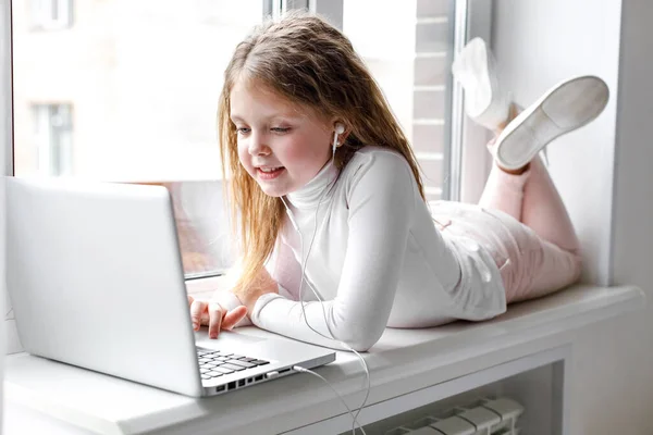 The girl at home communicates with friends on the Internet. Kids distance learning. Cute little girl using laptop at home. Education, online study, home studying, schoolgirl children lifestyle concept