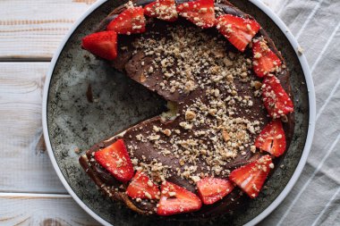 Siyah tabakta çilekli yuvarlak çikolatalı pasta. Hafif ahşap arka planda çikolatalı pasta tabağı. Bir dilim dilimlenmiş çikolatalı pasta. Tatlı yüksek kalorili yiyecekler.