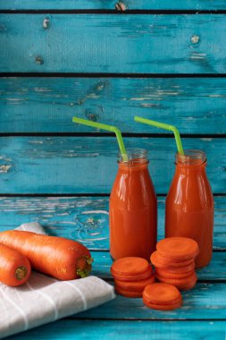 Parlak mavi arka planda taze sıkılmış havuç suyu. A vitamini, karoten ve Retinol kaynağı. Cam şişelerde sağlıklı sebze suyu. Vejetaryen ve vejetaryen yemekleri. Karşıtlık renkleri