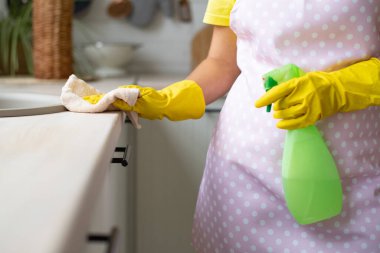 Temizlik, ev temizliği. Mutfakta hijyen ve temizlik var. Sarı lastik eldivenli ve önlüklü kız. El, masanın yüzeyini siler ve spreyi tutar.