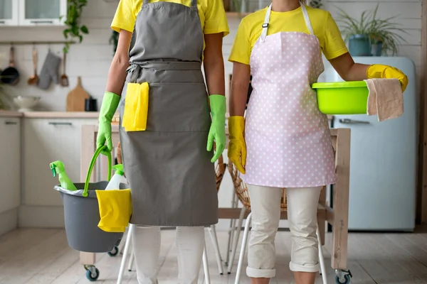 Two housemaids are cleaning the kitchen. General cleaning of the house. Professional cleaning service. Girls in special clothes, cleaning ladies, hold a bucket, vendace and a mop in their hands