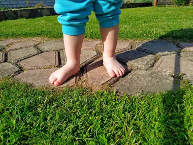 Mavi pantolonlu ve yalın ayaklı küçük bir çocuk yeşil çimlerin üzerinde duruyor.