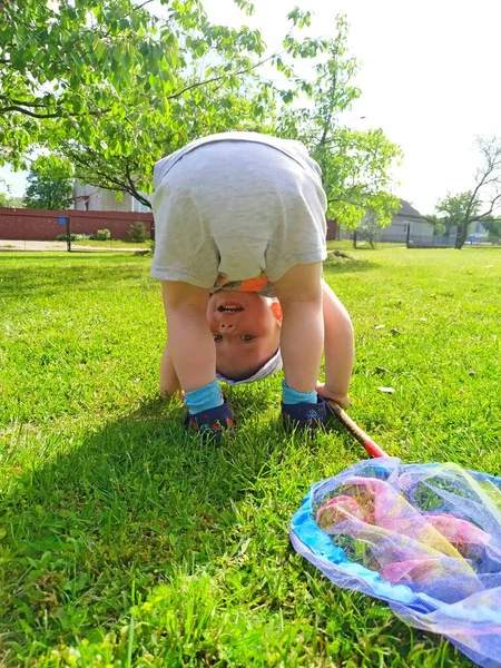 Felice piccolo ragazzo biondo con una rete blu è capovolto su un prato verde — Foto Stock