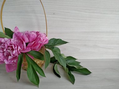 Açık ahşap masada hasır bir sepetin içindeki pembe şakayıklar.