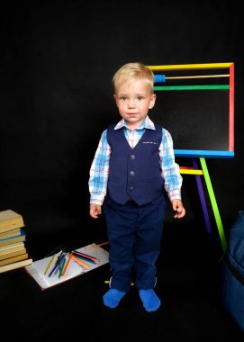 Mavi takım elbiseli, kara tahtanın yanında duran dalgın gülüşlü küçük çocuk.