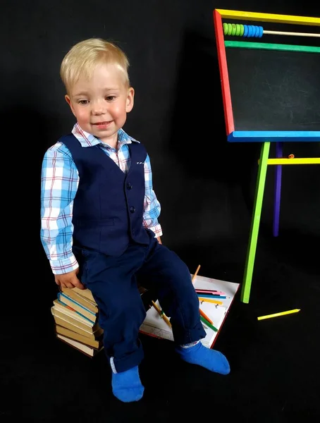 Niño pequeño en un traje azul con sonrisa tímida de pie junto a la pizarra —  Fotos de Stock