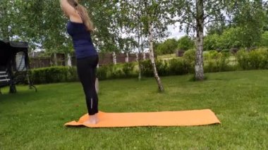 Genç bir kadın yazın bahçede yoga yapıyor. Surya namaskar bahçede
