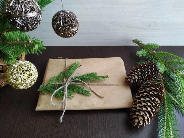 在枞树枝子和圣诞装饰品旁边用手工纸包着的圣诞礼物 — 图库照片