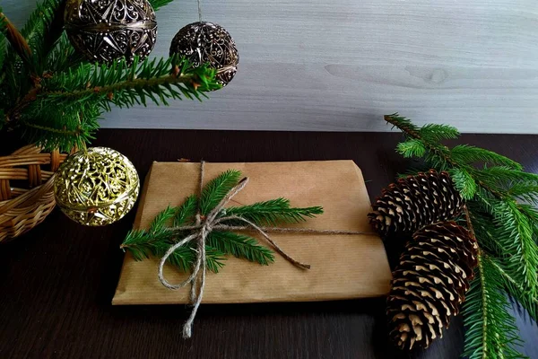 在枞树枝子和圣诞装饰品旁边用手工纸包着的圣诞礼物 — 图库照片