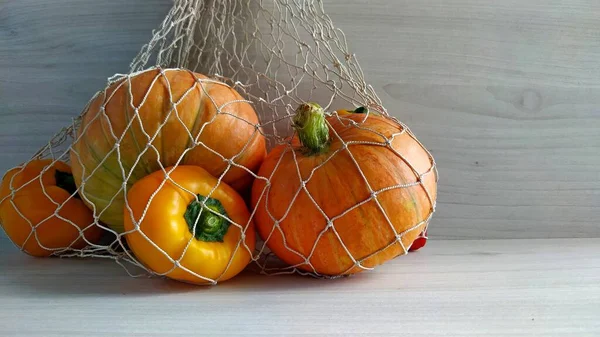 Erntezeit. Kürbisse und Paprika in einem Schnurbeutel auf hellem Holz-Hintergrund — Stockfoto