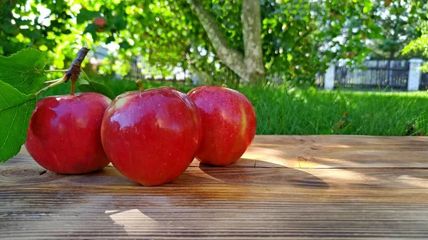 Tři červená zralá jablka s listy na dřevěném pozadí — Stock fotografie