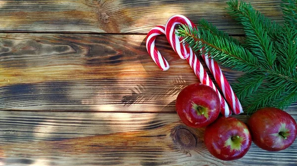 Έλατο κλαδιά, λαμπερά κόκκινα μήλα και γλειφιτζούρια Χριστουγέννων σε ξύλινο φόντο — Φωτογραφία Αρχείου