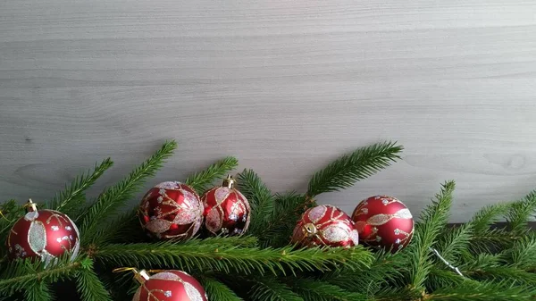 cut spruce branches with red christmas balls on dark wood background