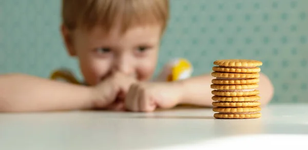 Sarışın çocuk gülümsüyor ve masada atıştırıyor.