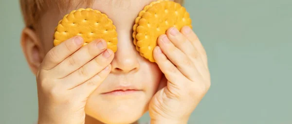 Çocuk elinde bir kurabiye tutuyor ve onunla gözlerini kapıyor.