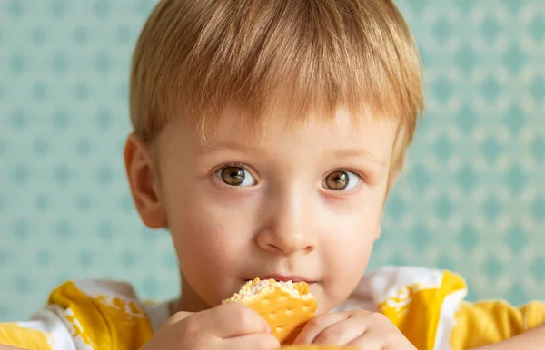 Sarışın çocuk gülümsüyor ve masada atıştırıyor.