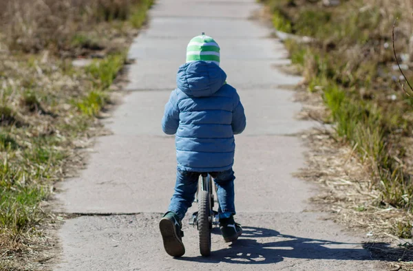 Bir çocuk pistte dengeli bisiklet sürüyor. Bahar havası. Güneş.