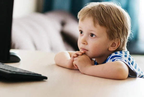 Sarı ceketli bir çocuk, evde bir masada oturuyor, bir dizüstü bilgisayara bakıyor, internetten öğreniyor, evde internet üzerinden öğreniyor. Teknoloji, okul, bilgi.