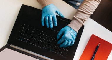 Ev bilgisayarında çalışan bir adam korunmak için tek kullanımlık eldiven giyiyor. Coronavirüs salgını. Karantinaya alınmış bir iş adamı. Evde çalış. Evde kal..