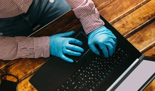 Ev bilgisayarında çalışan bir adam korunmak için tek kullanımlık eldiven giyiyor. Coronavirüs salgını. Karantinaya alınmış bir iş adamı. Evde çalış. Evde kal..