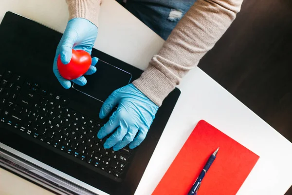 Ev bilgisayarında çalışan bir adam korunmak için tek kullanımlık eldiven giyiyor. Coronavirüs salgını. Karantinaya alınmış bir iş adamı. Evde çalış. Evde kal..