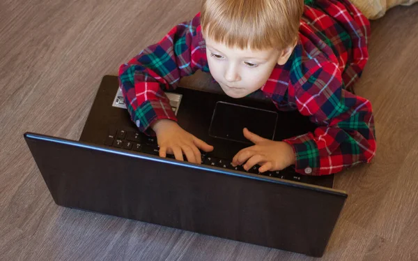 Çocuk evdeki aydınlık zeminde yatarken dizüstü bilgisayara bakıyor.