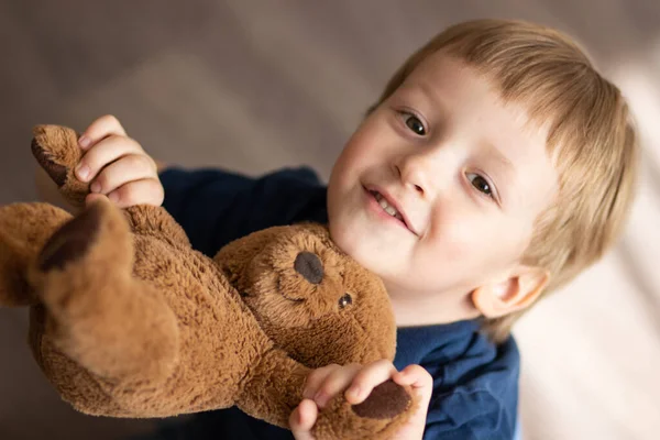 Sarı saçlı, gülümseyen, ayıyla oynayan güzel bir çocuk. yakın plan