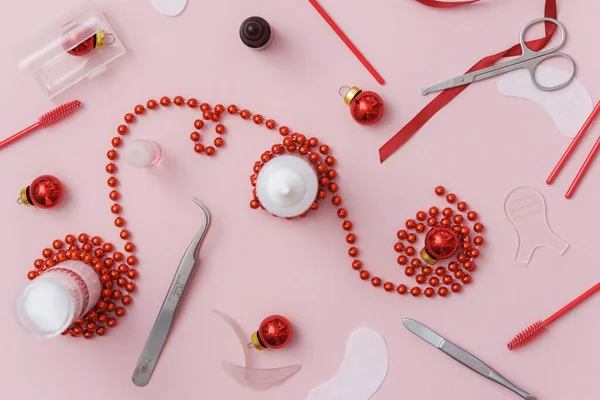 Güzellik salonu ve kirpik sanatları aletleri ve tedavi ürünleri Noel temalı pembe bir arka plan üzerinde üst görünüm. Tedavi için aletleri olan Noel ağacı oyuncakları. Boşluğu kopyala.