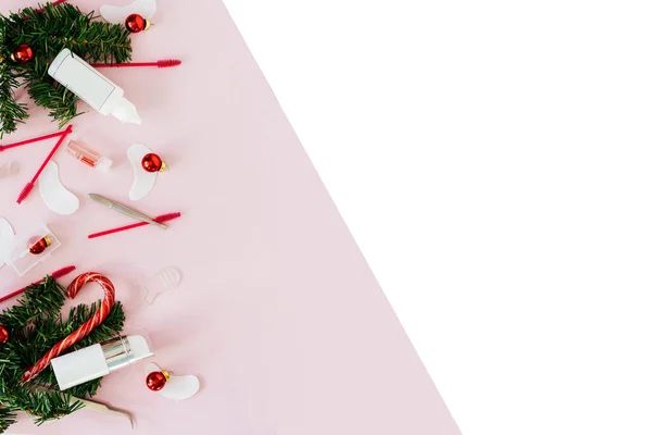 Güzellik salonu ve kirpik sanatçısı aletleri ve tedavi ürünleri sol tarafta, Noel temalı pembe beyaz arka planda bir çerçeve oluşturuyorlar. Tedavi için aletleri olan Noel ağacı oyuncakları. Anlaşıldı.