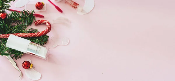 Güzellik salonu ve kirpik sanatçısı aletleri ve tedavi ürünleri sol tarafta, Noel temalı pembe arka planda bir çerçeve oluşturuyorlar. Şeker ve Noel oyuncakları ve tedavi araçları