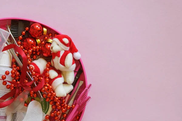 Güzellik salonu ve kirpik sanatçısı aletleri ve tedavi ürünleri sol tarafta, Noel temalı pembe arka planda bir çerçeve oluşturuyorlar. Tedavi için aletleri olan Noel ağacı oyuncakları. Boşluğu kopyala.