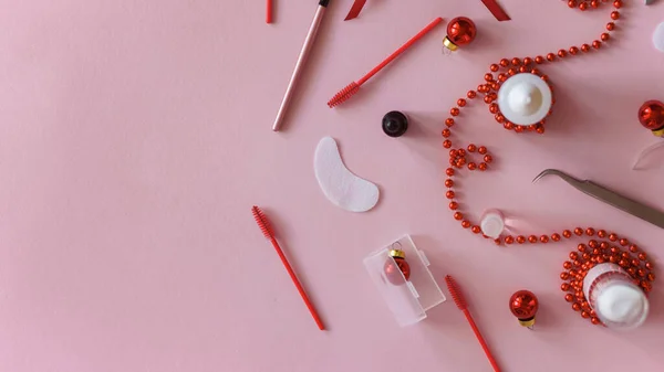 Güzellik salonu ve kirpik sanatçısı aletleri ve sağdaki tedavi ürünleri Noel temalı pembe arka planda bir çerçeve oluşturuyorlar. Tedavi için aletleri olan Noel ağacı oyuncakları. Boşluğu kopyala.