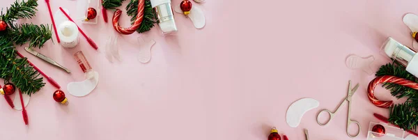 Güzellik salonu ve kirpik sanatçısı aletleri ve tedavi ürünleri sol tarafta, Noel temalı pembe arka planda bir çerçeve oluşturuyorlar. Şeker ve Noel oyuncakları ve tedavi araçları