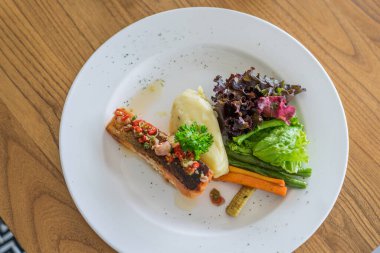 Beyaz tabakta patates püresi ve sebzeli somon bifteği.