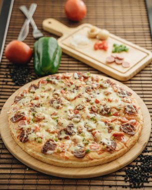 Etli peynirli pizza ve ahşap masada yemek malzemeleri.