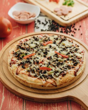 Ahşap masada yemek malzemeleri olan siyah biberli pizza.