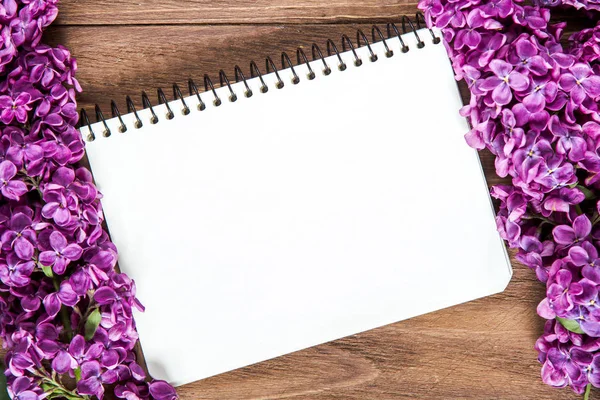 Bonita composición de un cuaderno en blanco y flores lila en la superficie de madera marrón — Foto de Stock