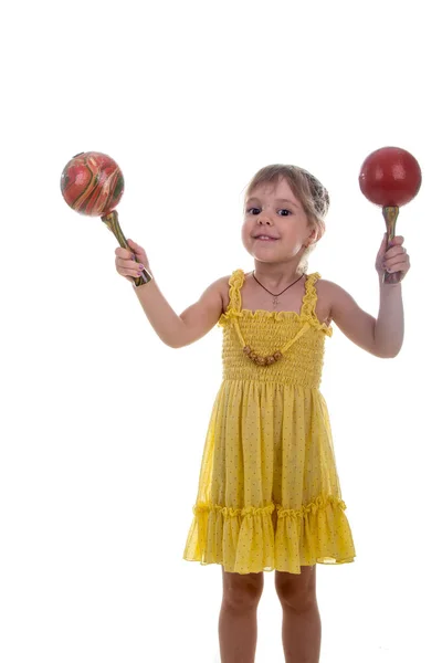 Klein meisje in een helder gele jurk met maracas in haar handen. Studio foto, helder witte achtergrond. — Stockfoto