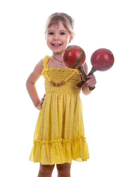 Klein meisje in een helder gele jurk maracas bedrijf in haar handen. Studio foto, helder witte achtergrond. — Stockfoto