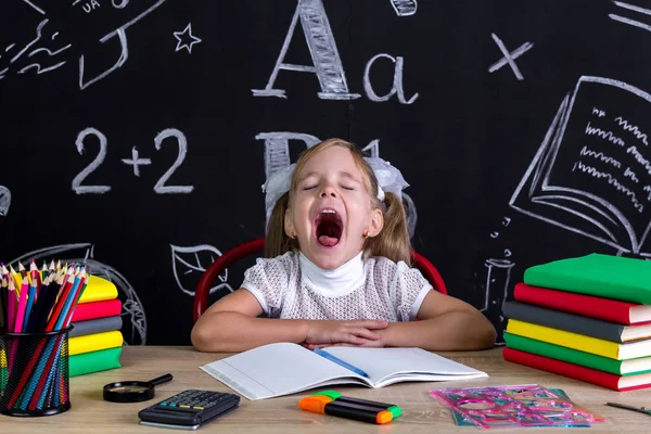 Niña bostezando sentada en el escritorio con libros, útiles escolares —  Fotos de Stock