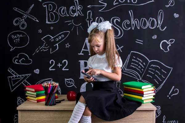 Colegiala desconcertada sentada en el escritorio con libros, útiles escolares, haciendo matemáticas con calculadora — Foto de Stock