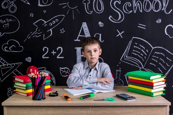 Graves excelente colegial sentado en el escritorio con libros, útiles escolares, con ambos brazos inclinados uno al otro — Foto de Stock